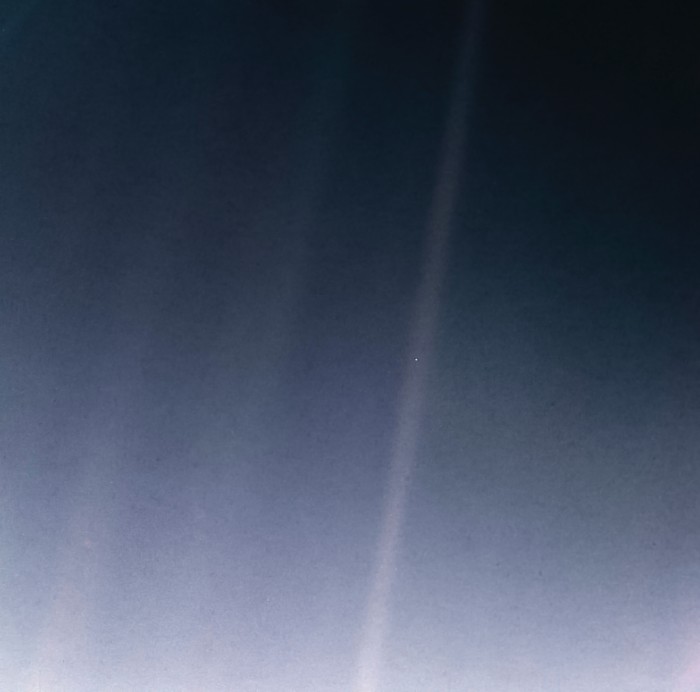 La Terre photographiée par Voyager 1 depuis plus de 6 milliards de kilomètres, apparaissant comme un minuscule point bleu pâle dans un rayon de lumière solaire diffusée